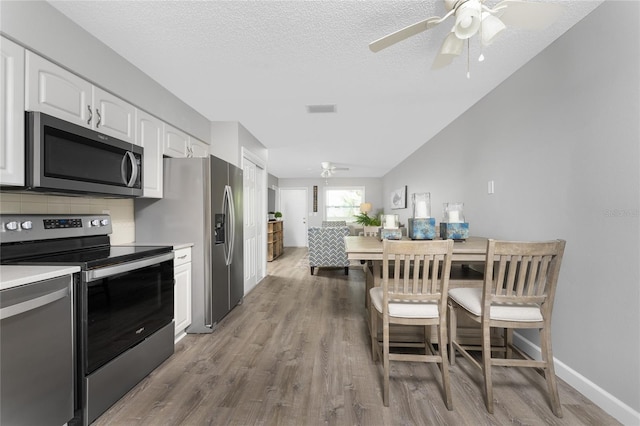 kitchen with stainless steel appliances, light countertops, white cabinetry, ceiling fan, and wood finished floors