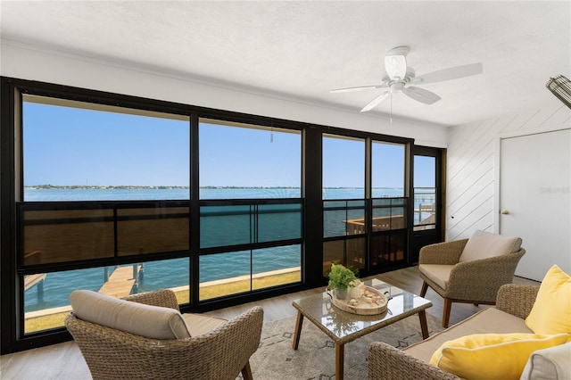 sunroom with a ceiling fan and a water view