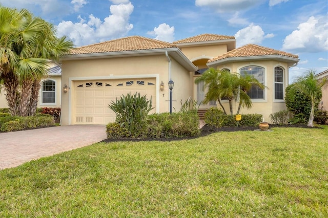 mediterranean / spanish-style home with a garage, a front lawn, decorative driveway, and stucco siding