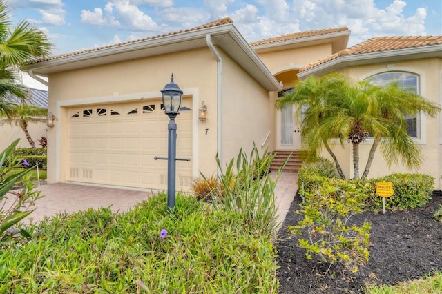 exterior space with a garage, decorative driveway, a tile roof, and stucco siding