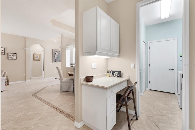 kitchen with light tile patterned floors, white cabinetry, baseboards, light countertops, and decorative columns