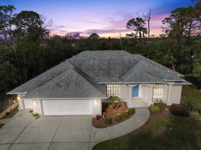 ranch-style house with a garage, roof with shingles, driveway, and stucco siding