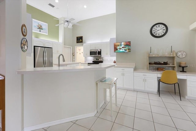 kitchen with stainless steel appliances, a high ceiling, white cabinetry, light countertops, and built in desk