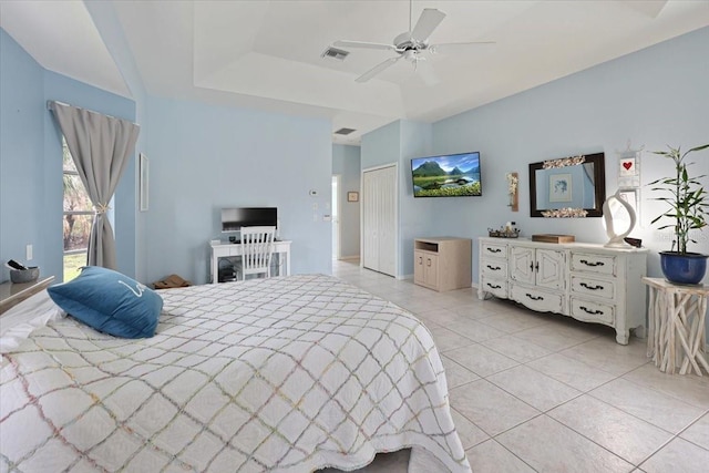 bedroom featuring light tile patterned floors, a tray ceiling, visible vents, and a ceiling fan