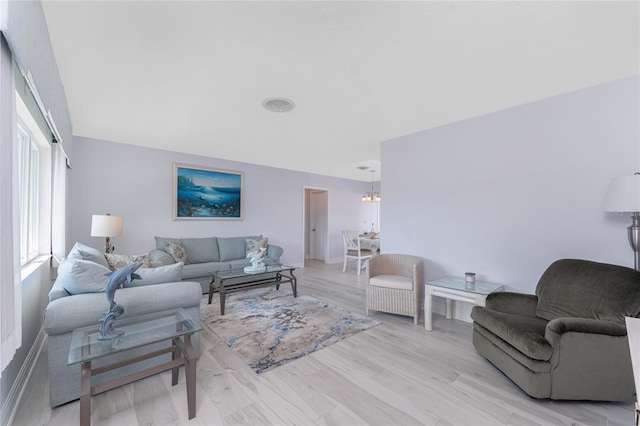 living room featuring light wood finished floors, visible vents, and a notable chandelier