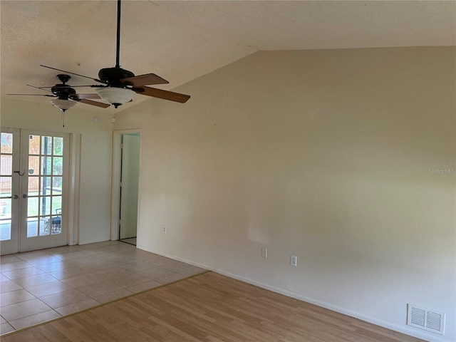 spare room with visible vents, vaulted ceiling, a textured ceiling, french doors, and light wood-style floors