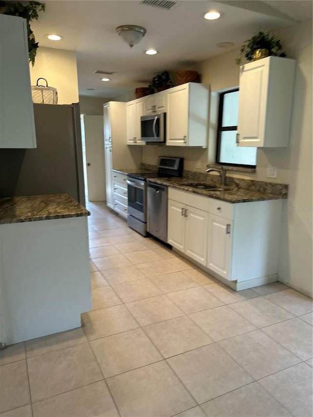 kitchen featuring appliances with stainless steel finishes, white cabinets, a sink, and dark stone countertops