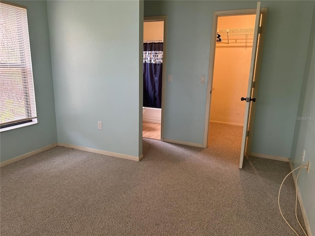 unfurnished bedroom with a closet, light colored carpet, a spacious closet, and baseboards