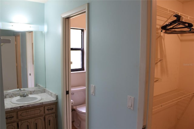 bathroom with toilet, a spacious closet, and vanity