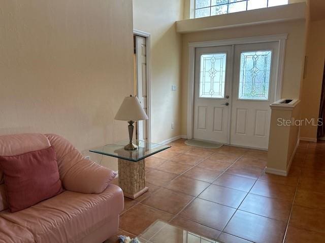 foyer with french doors, light tile patterned flooring, a towering ceiling, and baseboards