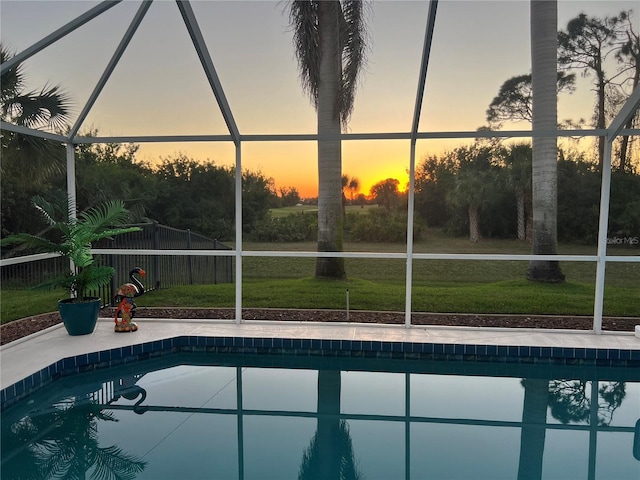 pool at dusk featuring glass enclosure, a yard, a patio, and an outdoor pool