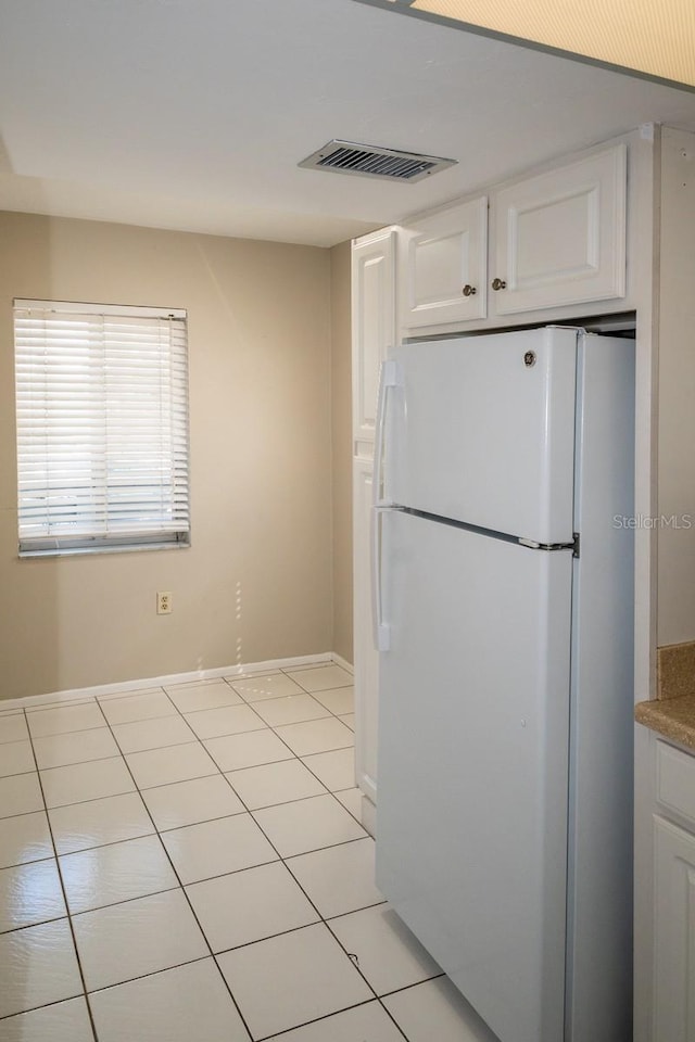 kitchen featuring light tile patterned floors, visible vents, freestanding refrigerator, white cabinetry, and baseboards