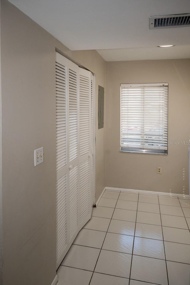 hallway featuring electric panel, visible vents, baseboards, and light tile patterned floors