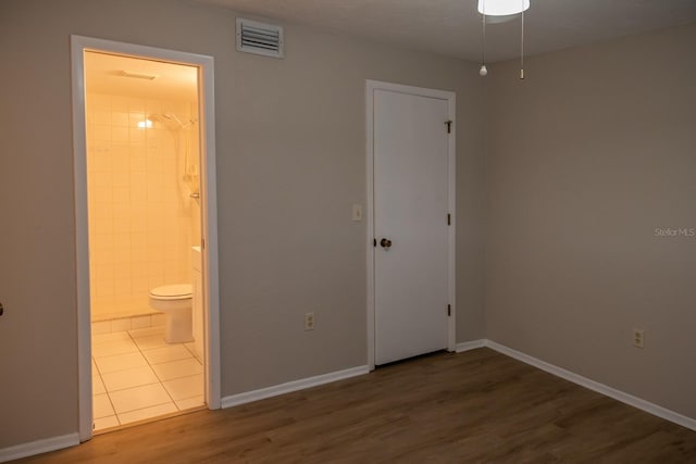 unfurnished bedroom with baseboards, visible vents, wood finished floors, and ensuite bathroom