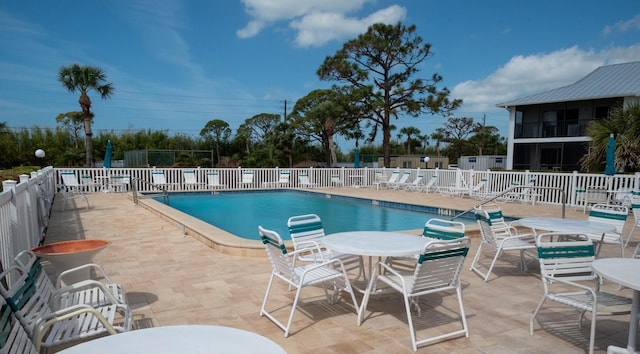 community pool with a patio area, fence, and outdoor dining area