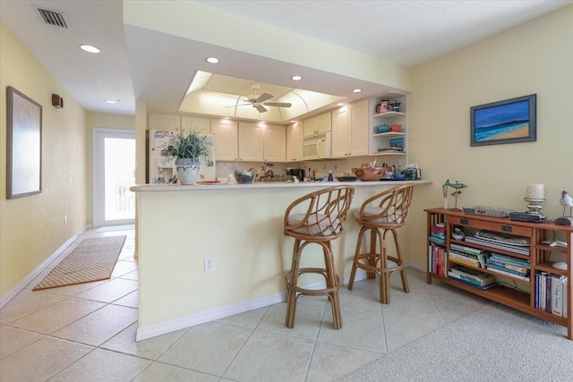 kitchen featuring light tile patterned floors, a peninsula, white microwave, and visible vents