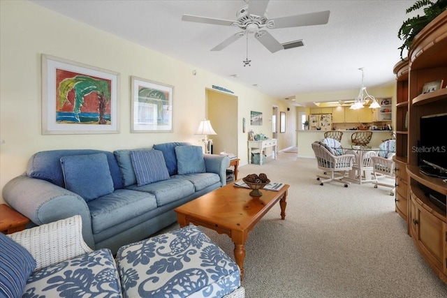 living room with ceiling fan with notable chandelier, visible vents, and light colored carpet