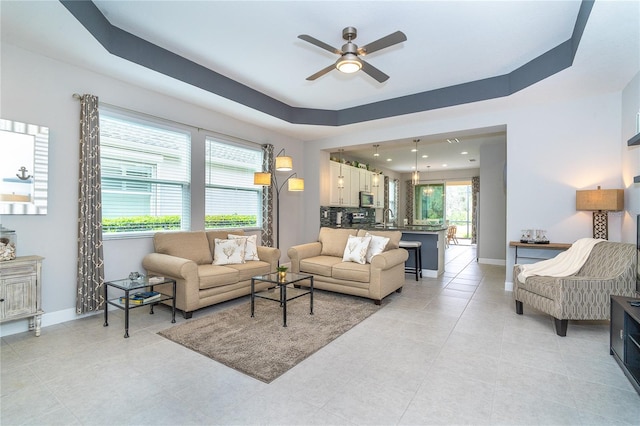 living room with light tile patterned flooring, recessed lighting, a ceiling fan, baseboards, and a tray ceiling