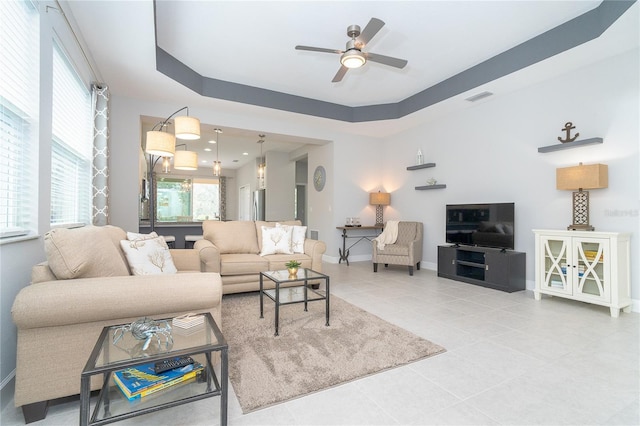 living room featuring tile patterned flooring, a ceiling fan, visible vents, baseboards, and a raised ceiling