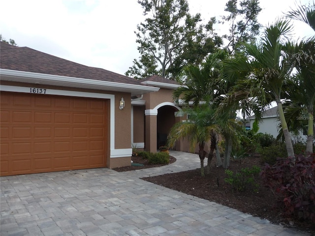 view of front of property with a shingled roof, decorative driveway, an attached garage, and stucco siding