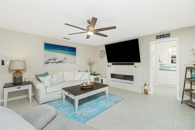 living room with light tile patterned floors, ceiling fan, visible vents, baseboards, and a glass covered fireplace