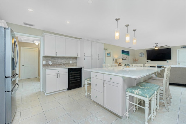 kitchen featuring wine cooler, visible vents, white cabinets, stainless steel fridge, and a kitchen bar