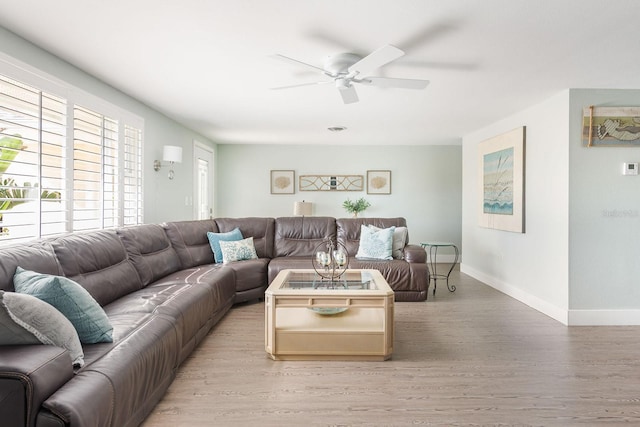 living room with light wood-type flooring, plenty of natural light, baseboards, and a ceiling fan