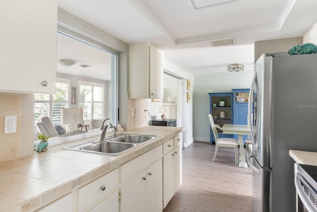 kitchen with visible vents, light wood-style flooring, appliances with stainless steel finishes, a tray ceiling, and a sink