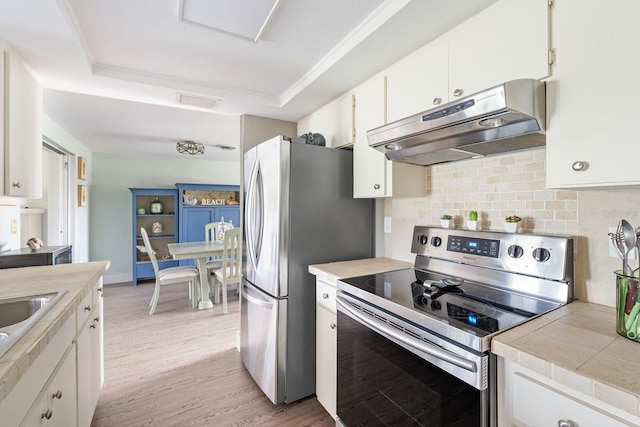 kitchen with light wood finished floors, appliances with stainless steel finishes, a raised ceiling, and under cabinet range hood