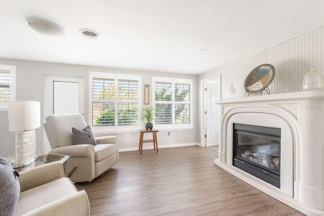 living area with a glass covered fireplace, visible vents, baseboards, and wood finished floors