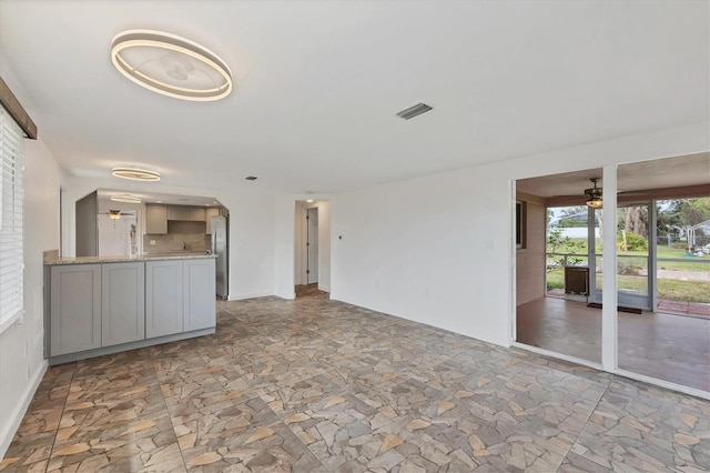 unfurnished living room with baseboards, visible vents, stone finish floor, and a ceiling fan