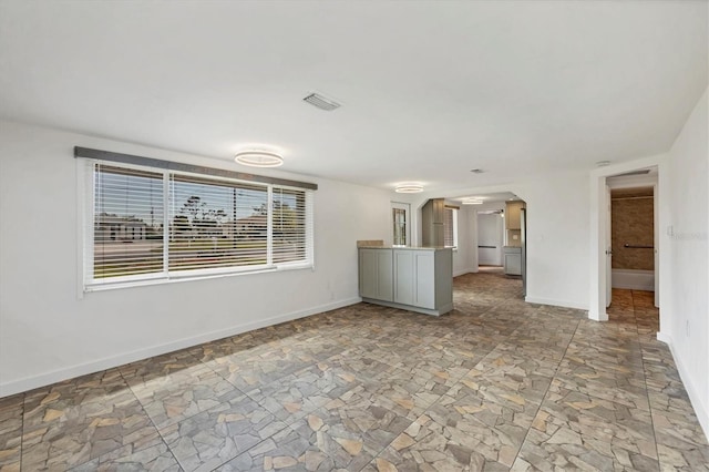 spare room with baseboards, visible vents, arched walkways, and stone finish flooring