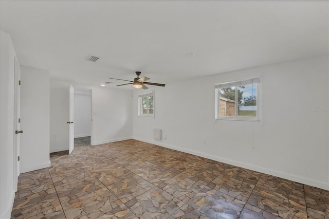 spare room with ceiling fan, a wealth of natural light, visible vents, and baseboards