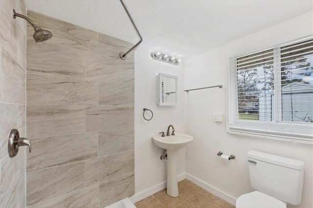 full bath with tiled shower, tile patterned flooring, toilet, and baseboards