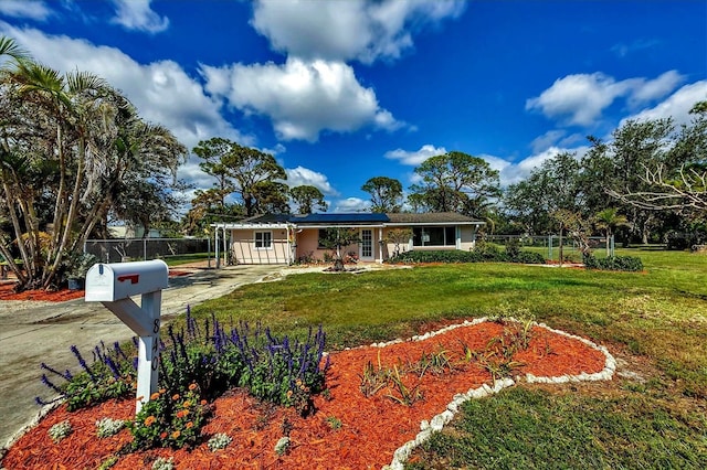 ranch-style house featuring a front yard, concrete driveway, fence, and solar panels