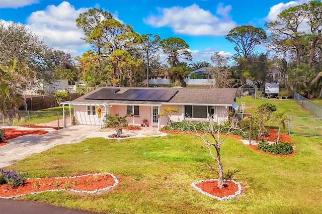 ranch-style home featuring roof mounted solar panels, fence, driveway, and a front lawn