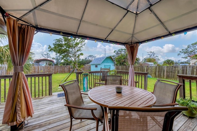 deck featuring a storage shed, a lawn, an outbuilding, a gazebo, and outdoor dining space