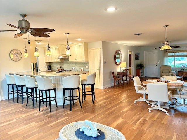 kitchen featuring tasteful backsplash, visible vents, light wood-style floors, and a kitchen breakfast bar