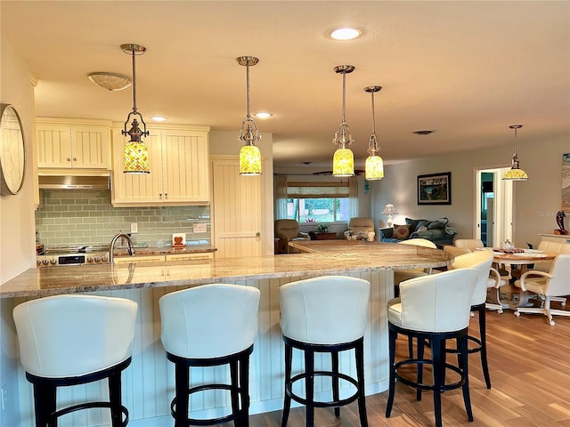 kitchen with light wood-style flooring, a breakfast bar area, open floor plan, light stone countertops, and backsplash