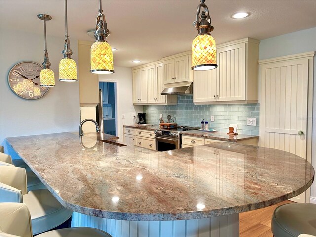 kitchen featuring a sink, range hood, stainless steel electric range, a kitchen bar, and backsplash