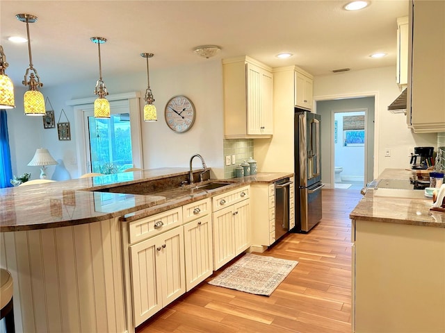 kitchen featuring range hood, freestanding refrigerator, a sink, light wood-type flooring, and a peninsula