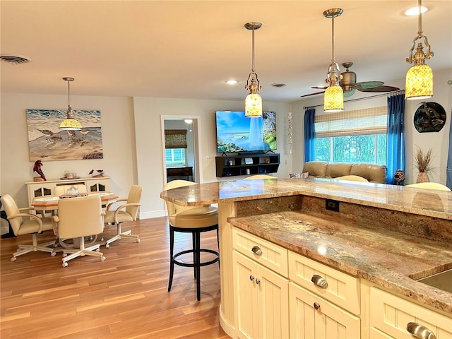 kitchen with visible vents, open floor plan, hanging light fixtures, light stone countertops, and light wood-type flooring