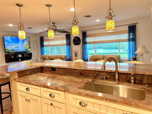 kitchen featuring stone countertops, a sink, visible vents, open floor plan, and hanging light fixtures