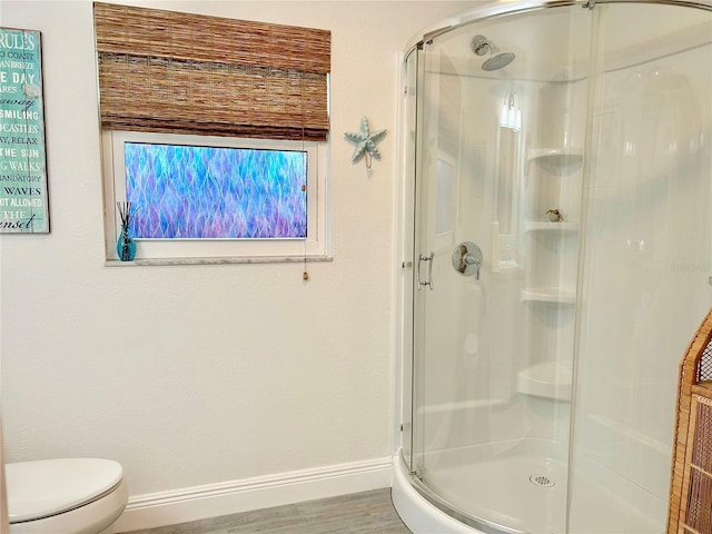 bathroom with a stall shower, wood finished floors, toilet, and baseboards