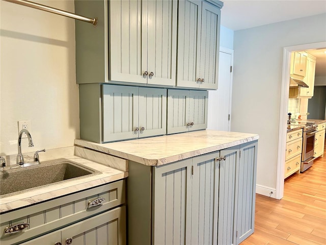 kitchen featuring gray cabinets, light countertops, light wood-style floors, a sink, and stainless steel gas range oven