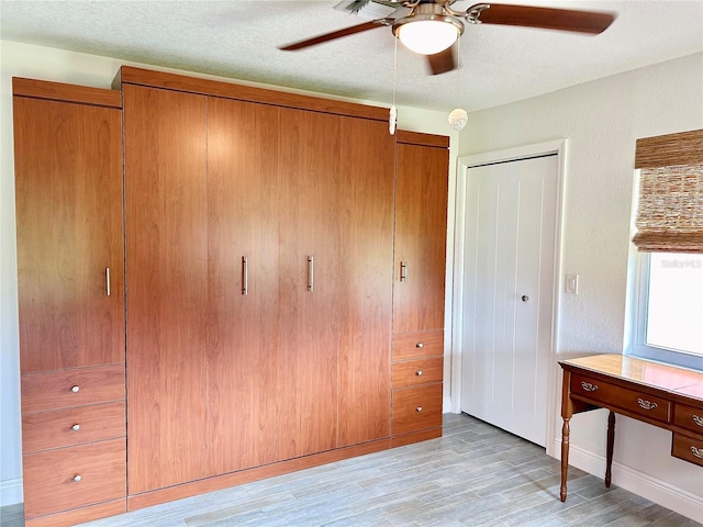 unfurnished bedroom with a textured ceiling, light wood-style flooring, and a ceiling fan