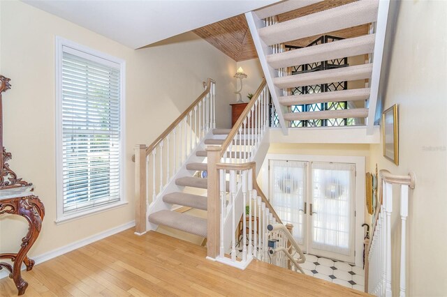 stairway with french doors, wood finished floors, and baseboards