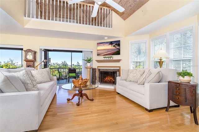 living area featuring light wood-type flooring, a wealth of natural light, ceiling fan, and a lit fireplace