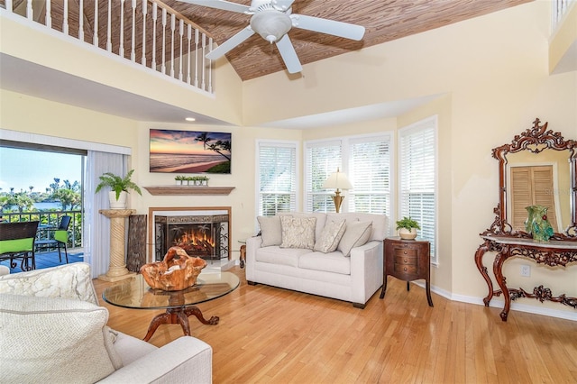 living area with a warm lit fireplace, ceiling fan, a towering ceiling, baseboards, and light wood finished floors