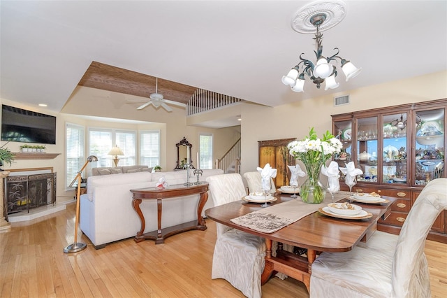 dining space featuring a fireplace with raised hearth, light wood-style flooring, visible vents, a healthy amount of sunlight, and stairs